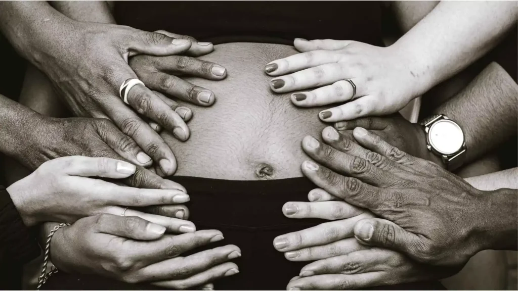 Hands from diverse individuals gently placed on a pregnant belly, symbolizing unity, hope, and success after fertility treatments.