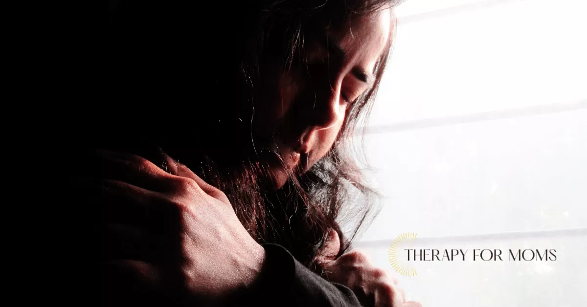 Mother with eyes closed holding herself in a moment of overwhelm, symbolizing postpartum emotional struggle.
